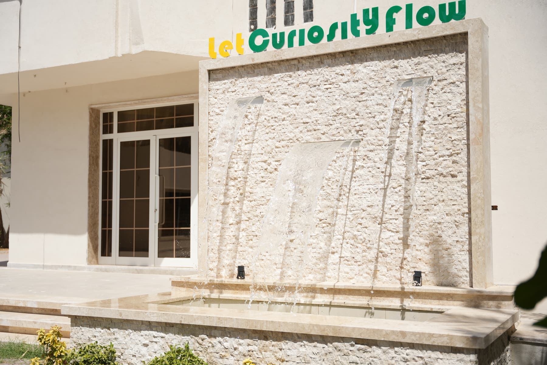 The school's water wall, lettered “Let Curiosity Flow”
